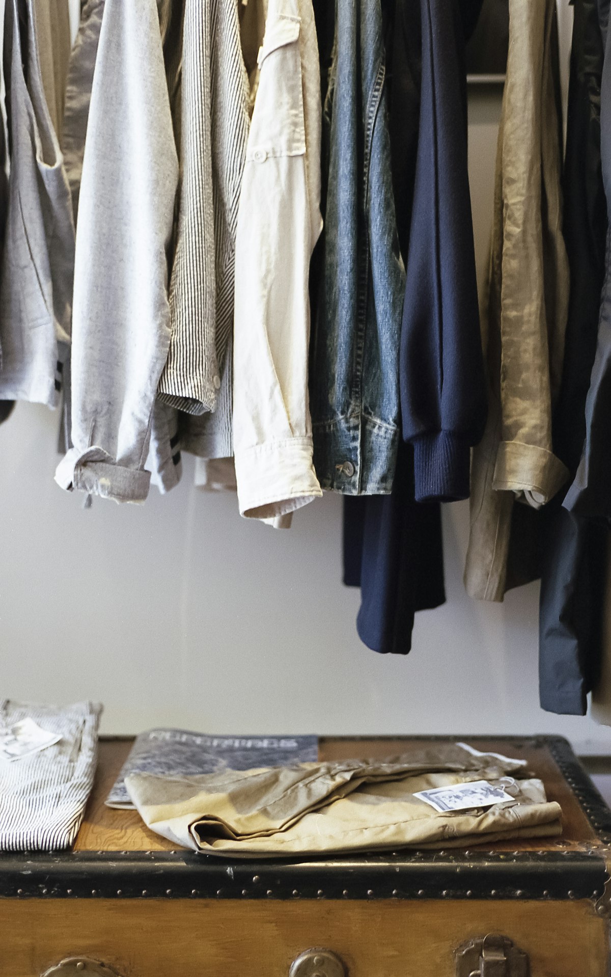 Curated wardrobe of shirts and denim hanging above a vintage trunk
